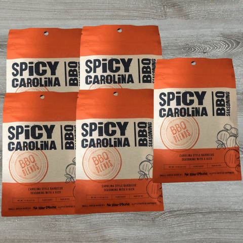 Five packs of Spicy Carolina BBQ Seasoning with vinegar and pepper blend on a wooden table.