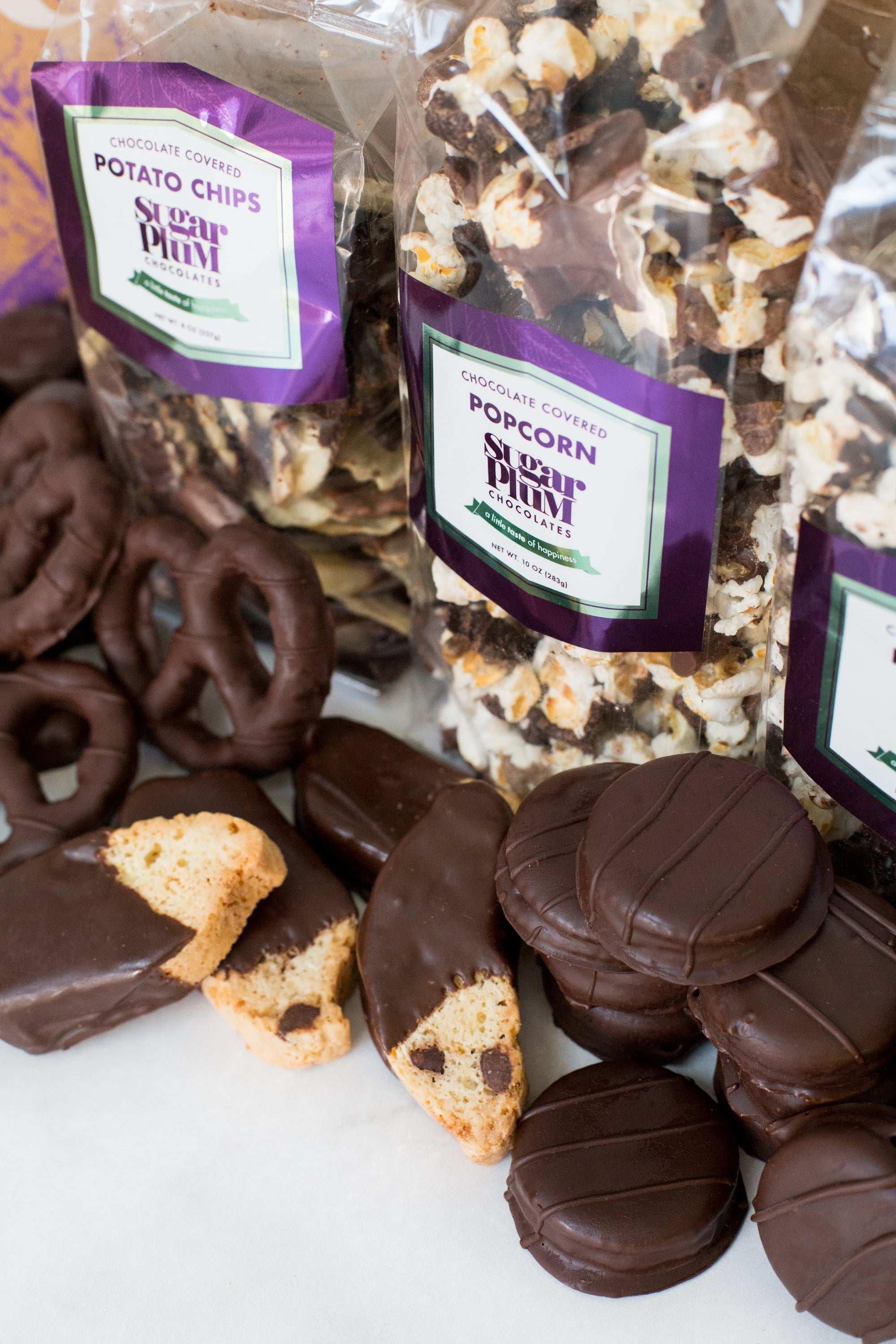 Assortment of handcrafted dark chocolate snacks including pretzels, cookies, and popcorn from Sugar Plum's gourmet gift box.