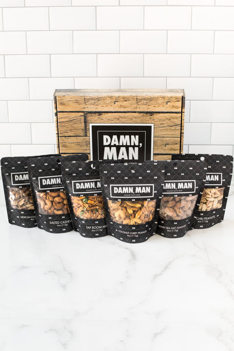 Manly Nut Box with six bags of assorted hand-crafted nuts arranged in front of a rustic gift box.