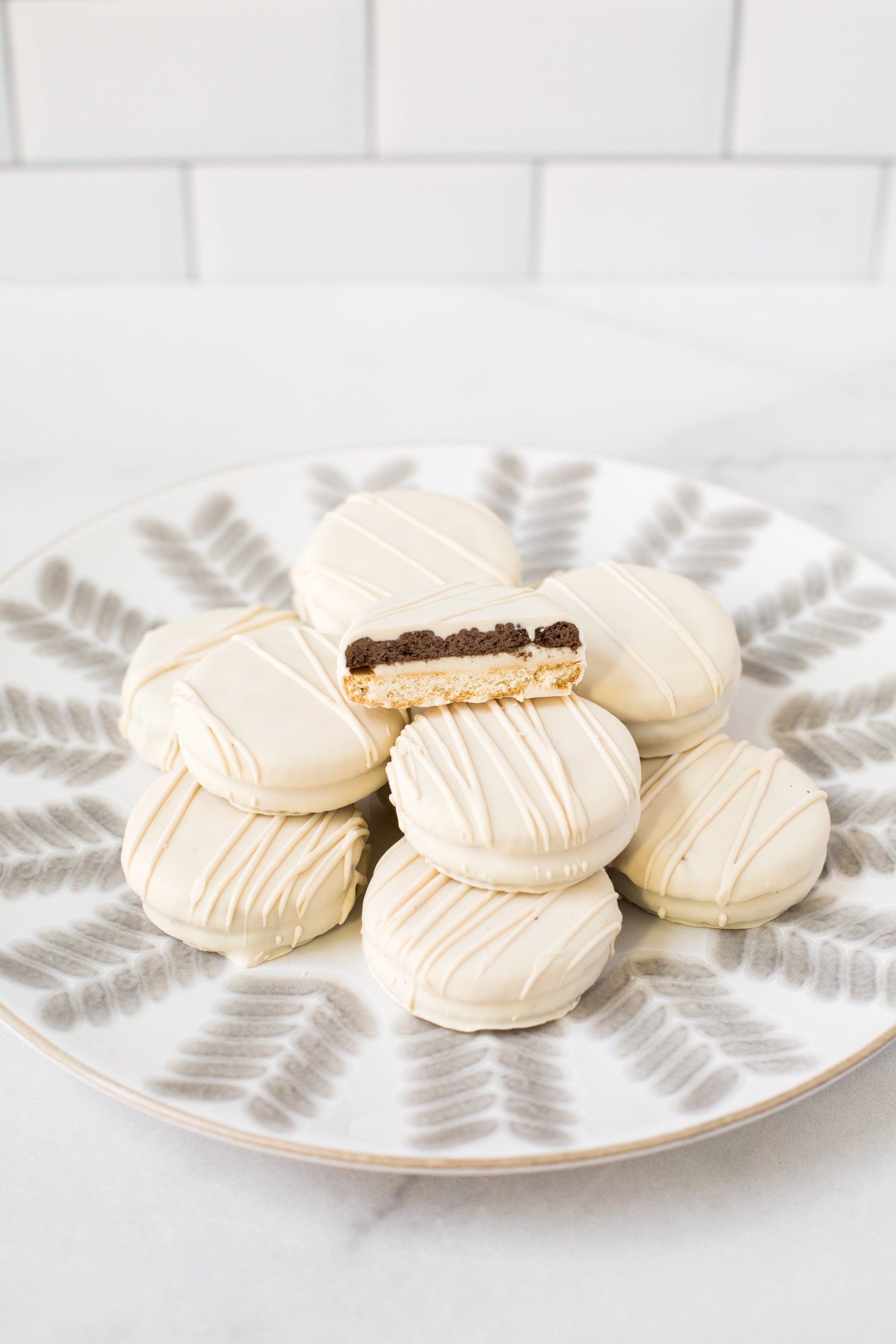 White chocolate-covered sandwich cookies arranged on a decorative plate, with one cookie showing a rich filling.
