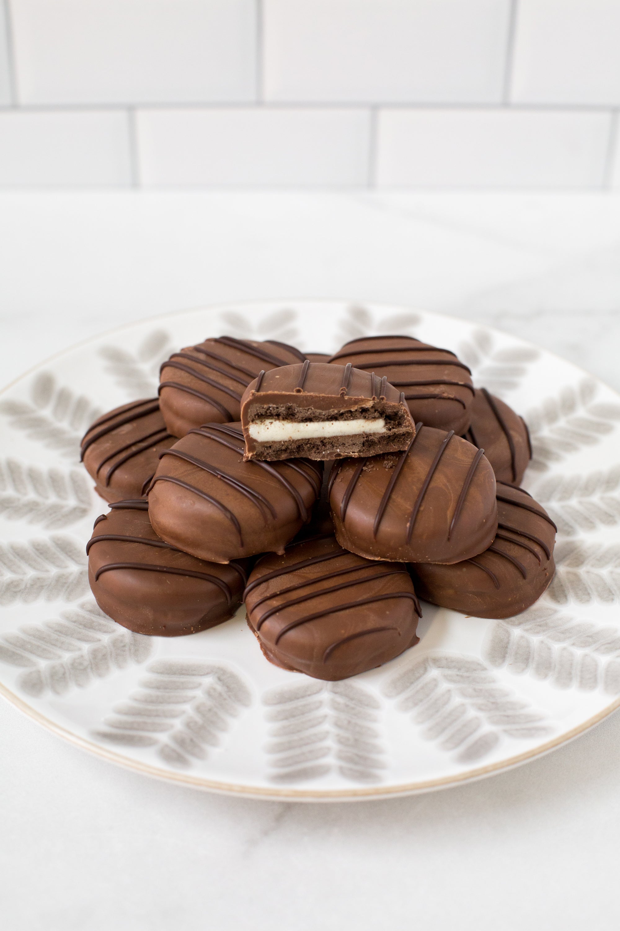 Plate of gourmet chocolate-covered sandwich cookies with a bite taken out of one, showcasing creamy filling and rich chocolate coating.