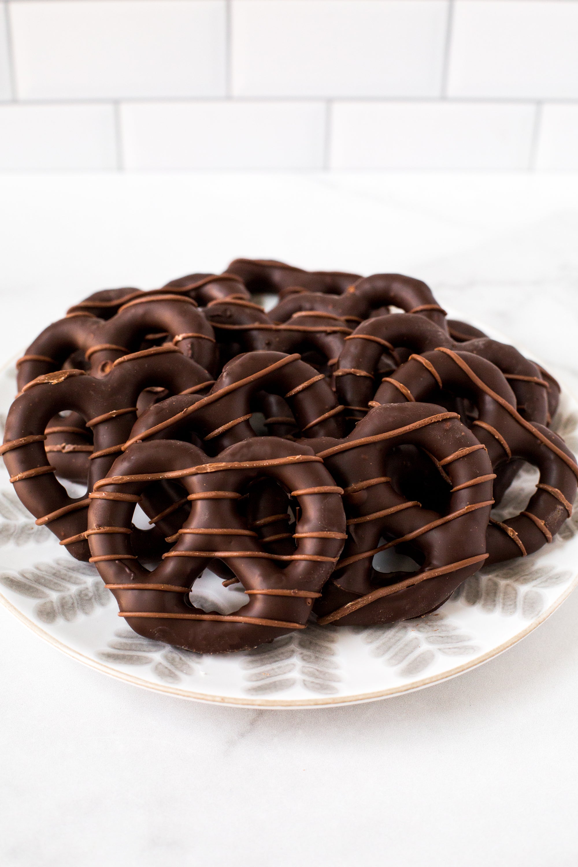 Chocolate-covered pretzels on a decorative plate, drizzled with chocolate, perfect for gifting or snacking.