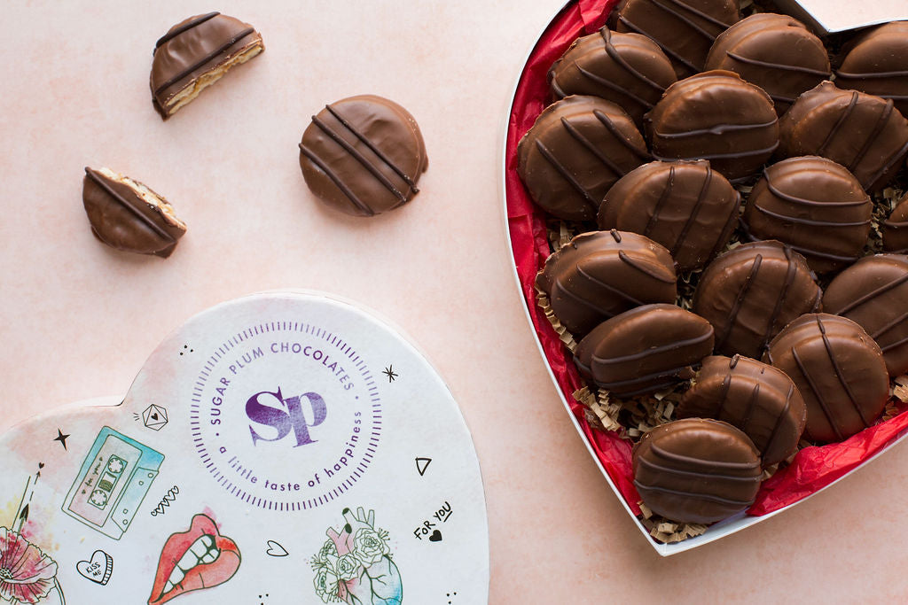Heart-shaped box of handcrafted milk chocolate-covered peanut butter crackers from Sugar Plum, presented on a light background.