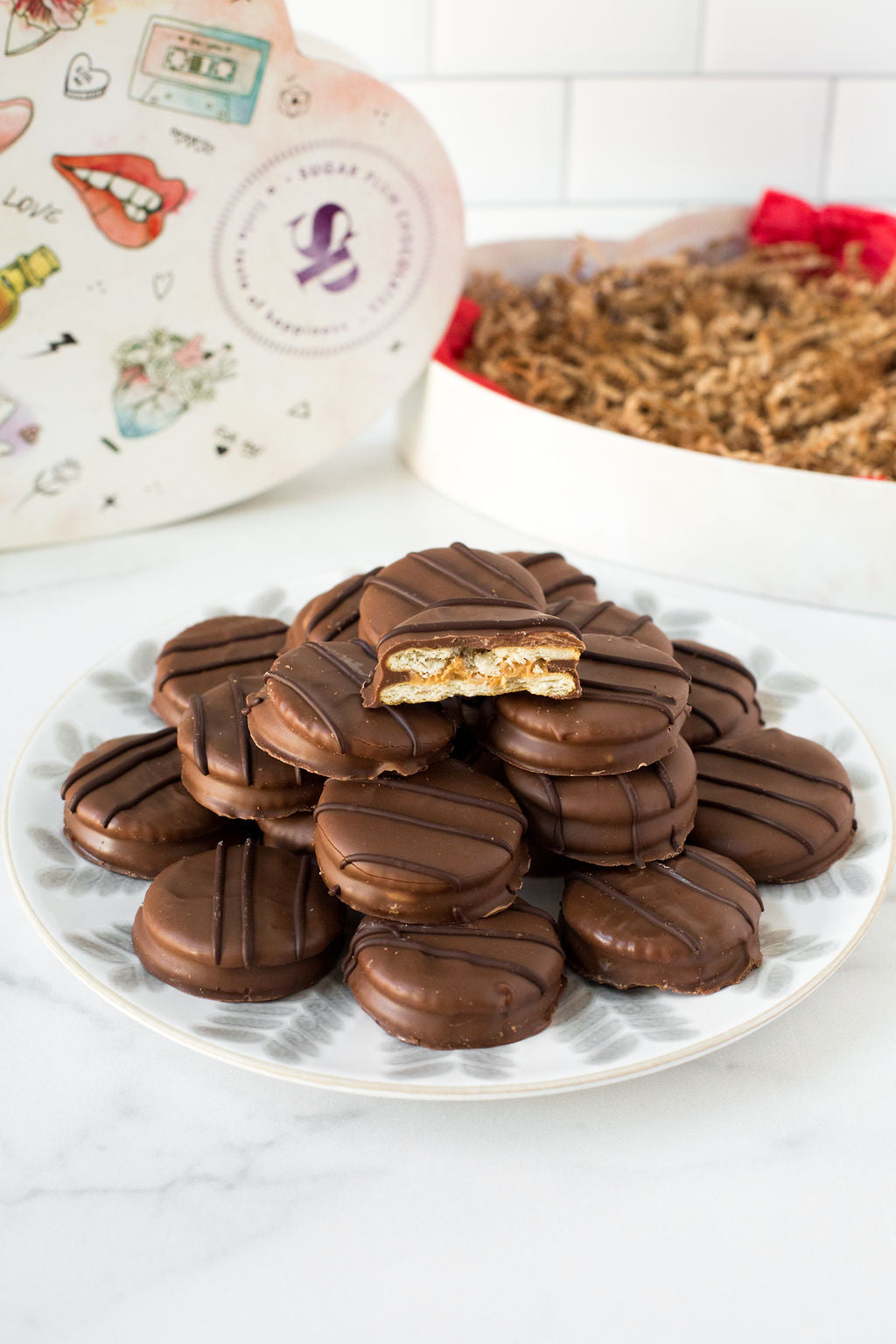 Milk chocolate-covered peanut butter cracker cookies on a plate, with a heart-shaped box in the background.