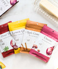 Four-pack of Butter Seasonings with flavors Lemon Garlic, Umami Butter, Sun-Dried Tomato, and Apple Cinnamon next to a stick of butter.