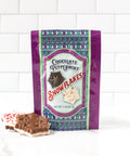 Chocolate Peppermint Snowflakes in festive packaging with snowflake-shaped chocolate pieces on a white tile background.