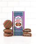 Milk chocolate covered holiday sandwich cookies with festive red and green stripes next to decorative packaging.