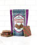 Milk chocolate covered graham crackers in festive holiday packaging with red and green stripes against a white tile background.