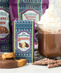 Decadent holiday chocolate treats display with caramel corn, biscotti, hot chocolate topped with whipped cream, and festive decor.