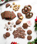 Assorted handcrafted holiday chocolates and treats on a festive background with greenery and poinsettias.