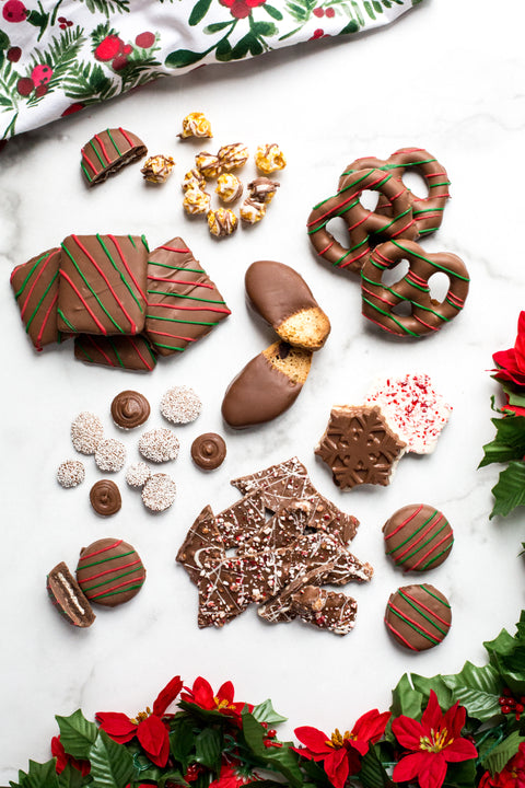 Assorted handcrafted holiday chocolates and treats on a festive background with greenery and poinsettias.