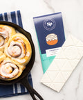 Cinnamon Roll White Chocolate Bar with skillet cinnamon rolls on marble background.