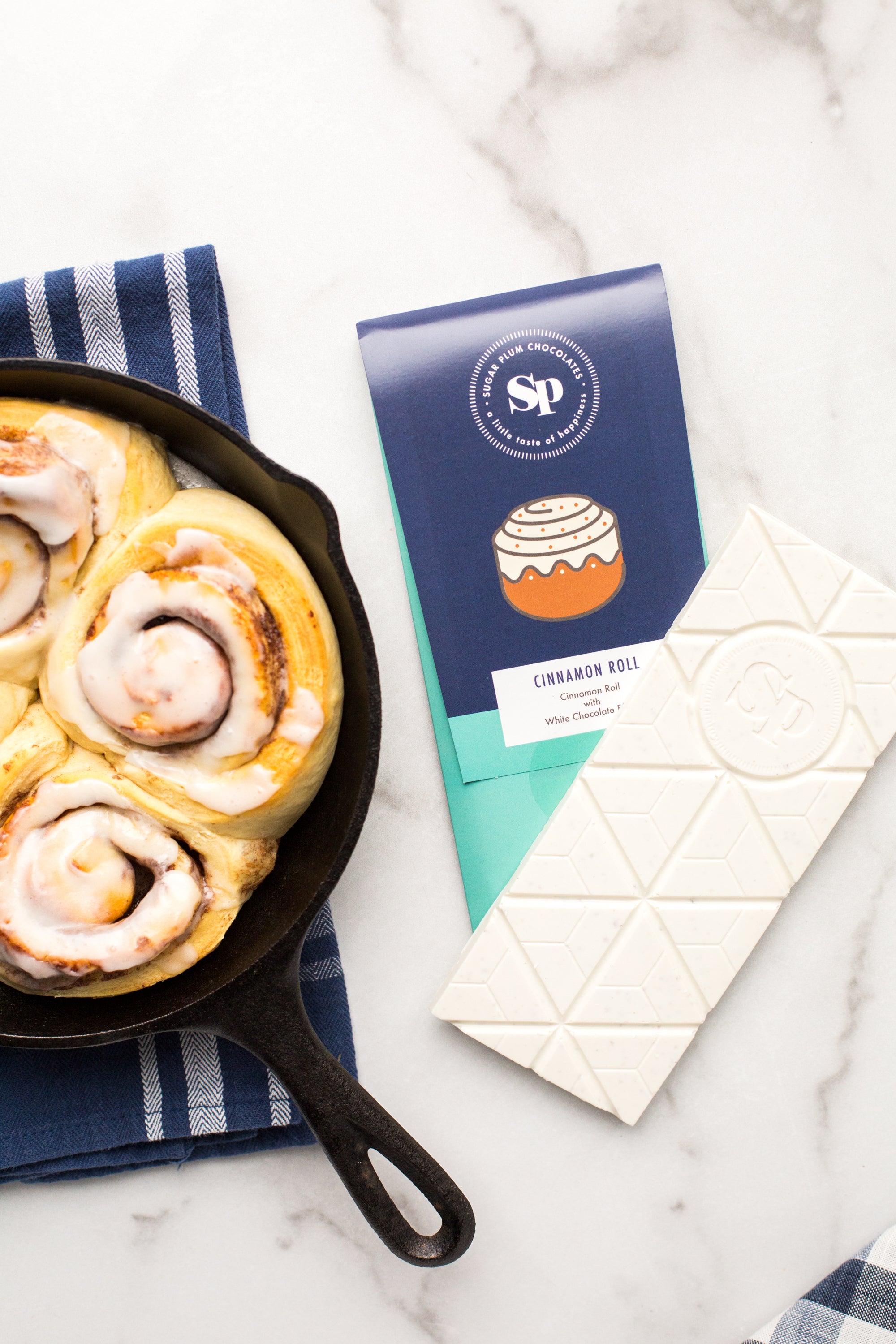 Cinnamon Roll White Chocolate Bar with skillet cinnamon rolls on marble background.