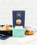 "Sugar Plum's Cinnamon Roll White Chocolate Bars with sticky buns in background"