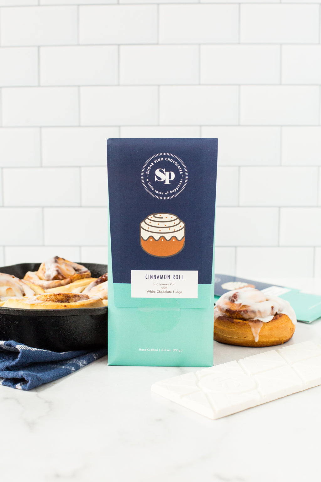 "Sugar Plum's Cinnamon Roll White Chocolate Bars with sticky buns in background"
