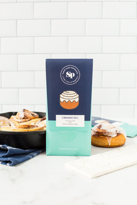 "Sugar Plum's Cinnamon Roll White Chocolate Bars with sticky buns in background"
