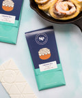 Cinnamon roll white chocolate bars next to freshly baked cinnamon rolls in a skillet.