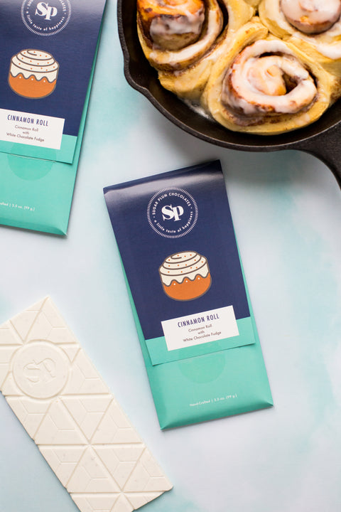 Cinnamon roll white chocolate bars next to freshly baked cinnamon rolls in a skillet.