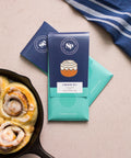 Cinnamon Roll White Chocolate Bars with graham cracker and sticky bun flavors beside fresh cinnamon rolls in a skillet.