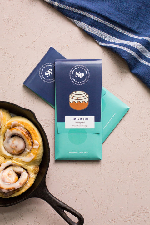 Cinnamon Roll White Chocolate Bars with graham cracker and sticky bun flavors beside fresh cinnamon rolls in a skillet.