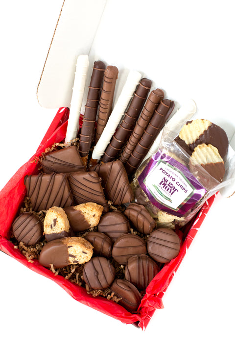 Gourmet chocolate gift box with chocolate-covered potato chips, cookies, pretzels, and hand-dipped treats in festive packaging.