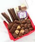 Gourmet chocolate gift box with chocolate-covered pretzels, potato chips, cookies, and assorted treats on a red tissue layer.