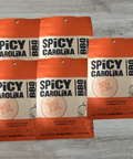 Five packs of Spicy Carolina BBQ Seasoning with vinegar and pepper blend on a wooden table.
