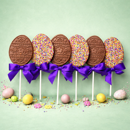 Chocolate egg pops with colorful sprinkles and purple ribbons on a light green background