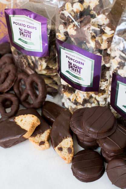 Assortment of handcrafted dark chocolate snacks including pretzels, cookies, and popcorn from Sugar Plum's gourmet gift box.