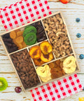 Gourmet dried fruit and nut tray on wooden platter with apricots, dates, kiwis, peaches, apples, cashews, and smoked almonds.