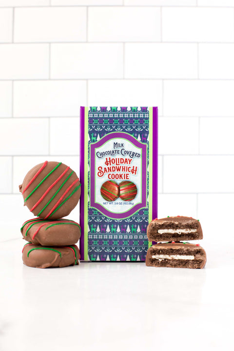 Milk chocolate covered holiday sandwich cookies with festive packaging and stack of cookies on a tiled background