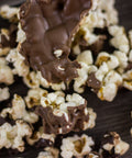 Gourmet chocolate-covered popcorn with milk and dark chocolate drizzles, a sweet and salty snack on a wooden surface.