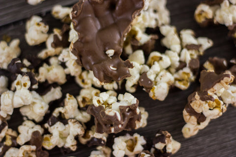 Gourmet chocolate-covered popcorn with milk and dark chocolate drizzles, a sweet and salty snack on a wooden surface.