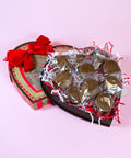Heart-shaped chocolate box with gold-wrapped chocolates on a pink background