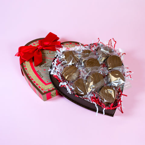 Heart-shaped chocolate box with gold-wrapped chocolates on a pink background