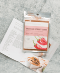 Mexican Street Corn seasoning packet with recipe cards on a gray surface, showcasing handcrafted spice blend for corn and hummus.