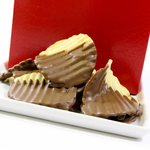 Chocolate-covered potato chips on a white plate with a red background, showcasing a sweet and salty snack blend.