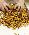 Hands mixing gourmet caramel popcorn with milk chocolate on a tray.