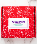 Red gift box adorned with white leaf patterns, featuring the Sugar Plum Chocolates logo on the front.