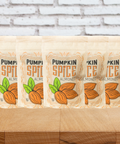 Five bags of kettle-cooked pumpkin spice almonds on a wooden table with a brick wall background.