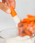 Person dipping carrot stick in creamy white sauce with bowl of carrots in background.
