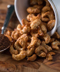 Gourmet coffee stout cashews spilling from a cup next to a spoon of ground coffee on a wooden surface.