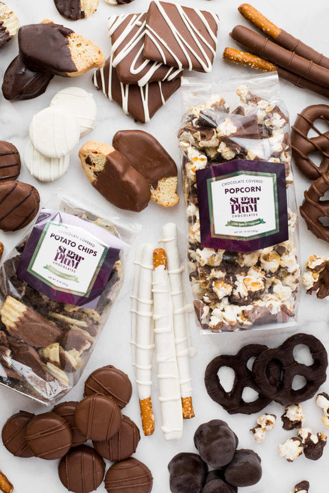 Assorted gourmet chocolates and snacks from Sugar Plum, featuring dark, milk, and white chocolate-covered treats in a holiday gift box display.