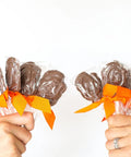 Two hands holding 10-pack of handcrafted gourmet milk chocolate turkey lollipops with orange bows, perfect for Thanksgiving.