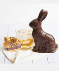 Whiskey-flavored dark chocolate toffee bunny with a glass of whiskey on a table.