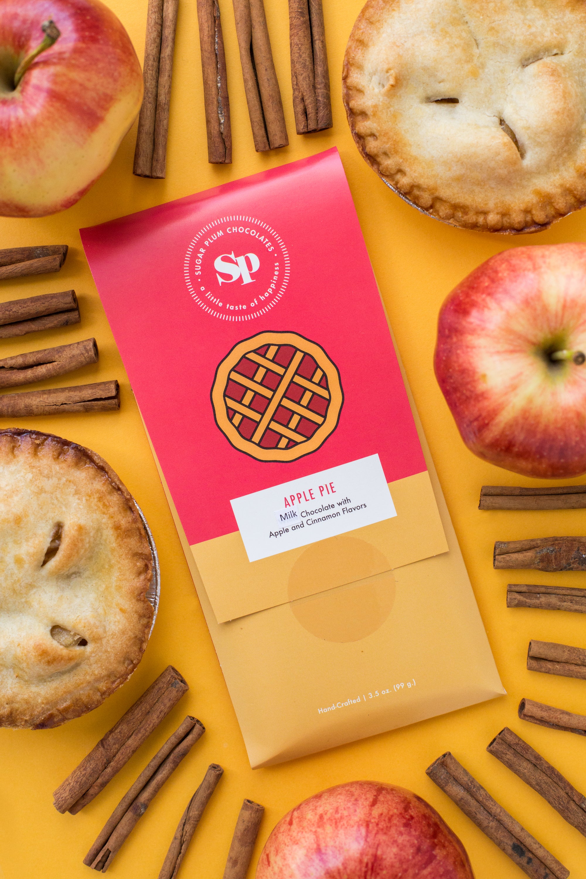 Nostalgic Apple Pie Chocolate Bar with fresh apples, cinnamon sticks, and mini pies on a vibrant yellow background.
