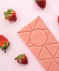Strawberry Cheesecake White Chocolate Bar with fresh strawberries on a pink background.