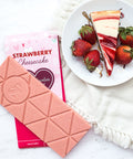 Strawberry Cheesecake White Chocolate Bar with fresh strawberries and cheesecake slice on a plate.