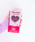Hand holding Strawberry Cheesecake White Chocolate Bar packaging against a white background