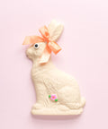 White bunny with an orange ribbon and pink accent lower in her body. 